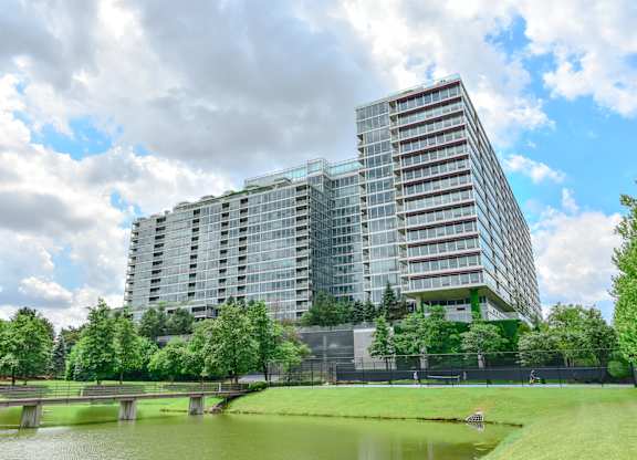 A modern glass building with a bridge over a pond in front.