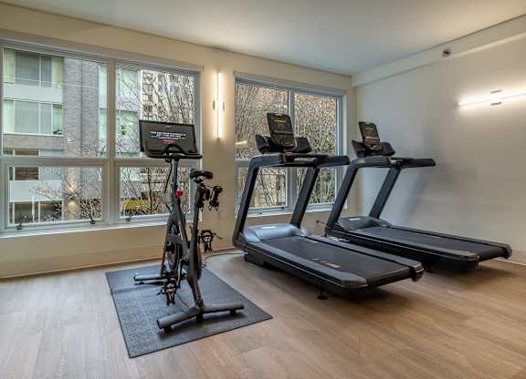 two treadmills and a bike in a room with windows
