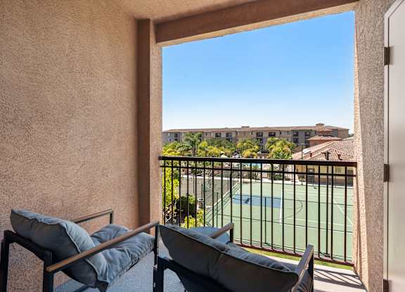 A balcony with a chair and a table overlooking a pool and buildings.