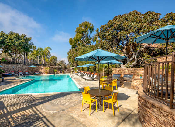 A pool area with a table and chairs and umbrellas.