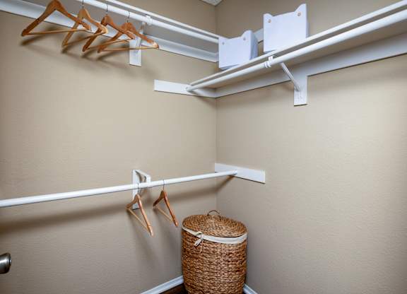 A white metal rod is mounted on a wall with clothes hangers and a basket underneath.