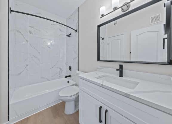 a bathroom with white cabinets and a white toilet next to a white bathtub with a shower