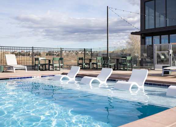 A pool with white chairs and a building in the background.