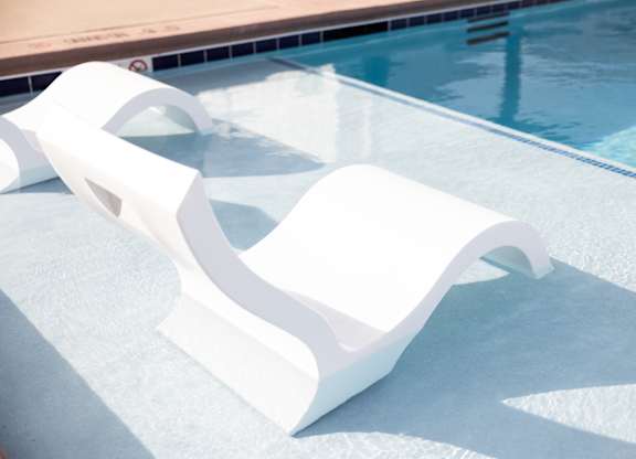 A white sun lounger is on the edge of a pool.