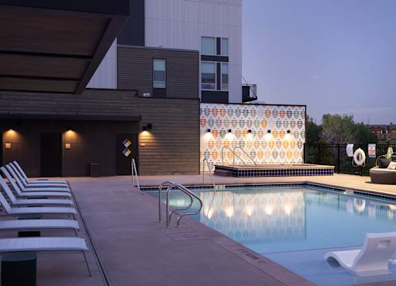 A pool with chairs and a building in the background.