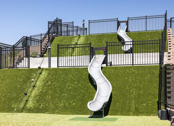A playground with a white slide and black fencing.