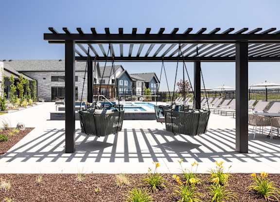 A patio with a pergola and chairs is surrounded by a garden.