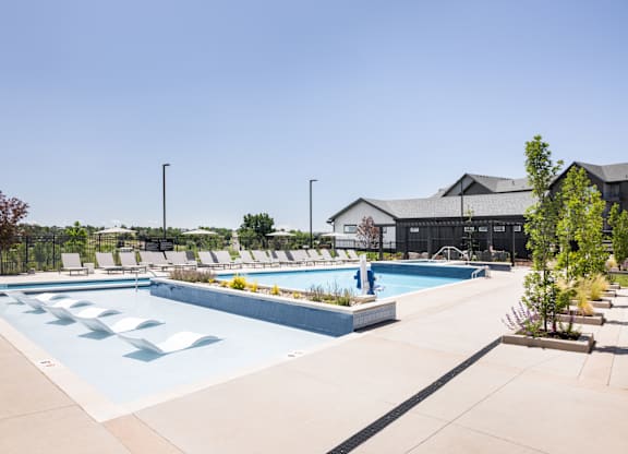 A large outdoor swimming pool with lounge chairs and a building in the background.