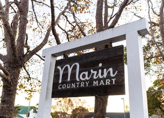 A sign for Marin Country Mart is displayed on a tree.