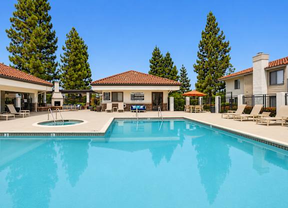 A large swimming pool in front of a house with a patio and trees in the background.