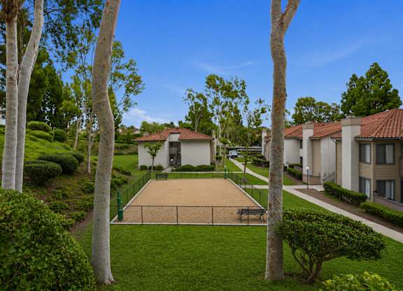 A tennis court is surrounded by trees and houses.