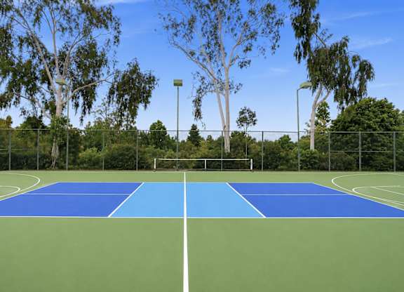 A tennis court with a blue top and green bottom is surrounded by trees.