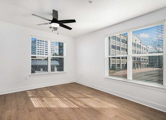 A room with a ceiling fan and two windows.