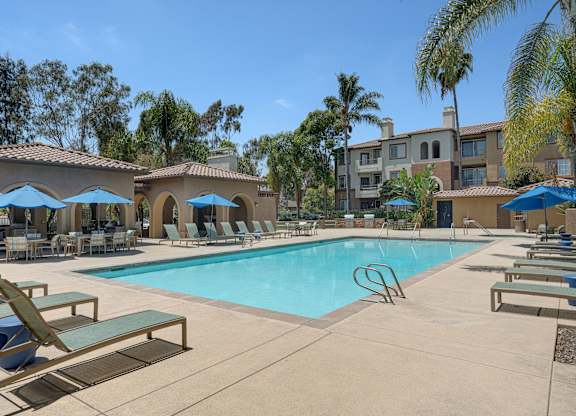 A swimming pool surrounded by sun loungers and umbrellas.