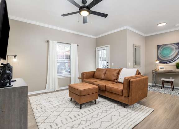 A living room with a brown couch, a television, and a ceiling fan at Clear Creek Meadows Apartments, Copperas Cove, 76522