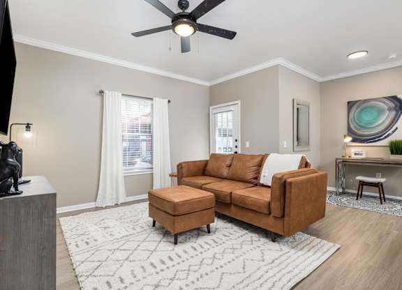 A living room with a brown couch, a television, and a ceiling fan at Clear Creek Meadows Apartments, Copperas Cove, TX, 76522