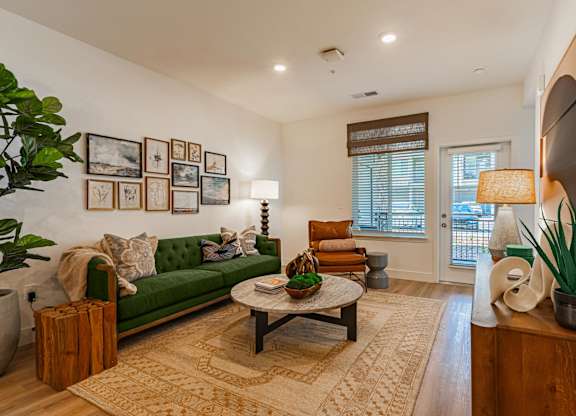 A living room with a green couch, a coffee table, and a large window.