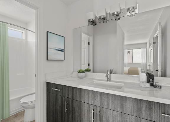 A modern bathroom with updated cabinetry and countertops with a large mirror.