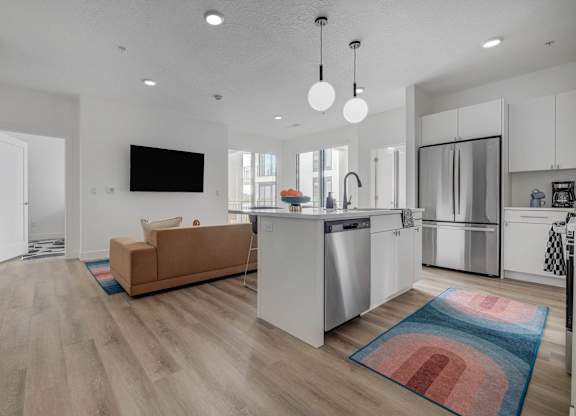 A modern kitchen with a brown sofa and a flat screen TV mounted on the wall.