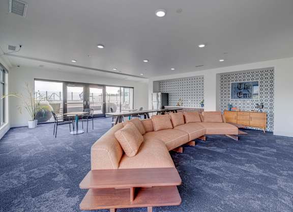 A long wooden table with a bench in front of a grey carpet.