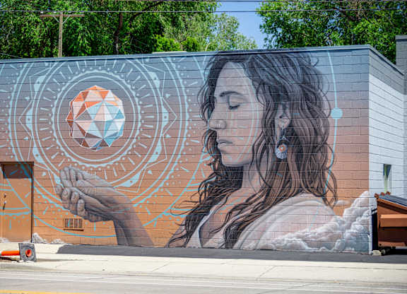 A mural of a woman holding a geometric object is painted on a building.