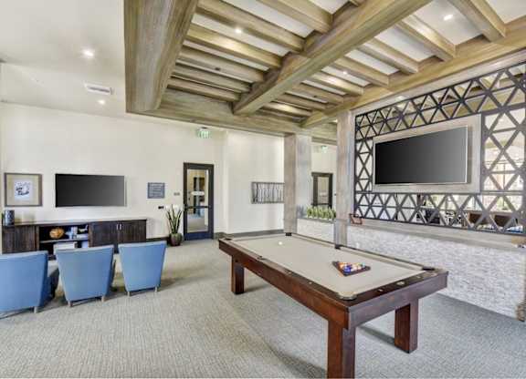 A billiard table is in the middle of a room with a TV and a wall with a picture frame.