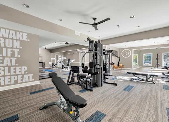 a gym with weights and a ceiling fan and a quote on the wall