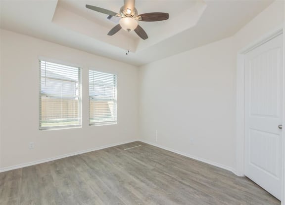a bedroom with a ceiling fan and two windows at The Village at Granger Pines, Texas
