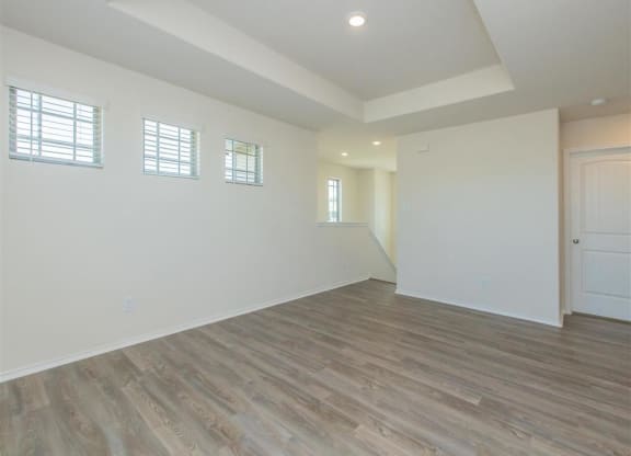 an empty living room with white walls and wood floors at The Village at Granger Pines, Conroe