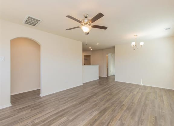 a living room with a ceiling fan and a kitchen in the background at The Village at Granger Pines, Conroe, TX 77302