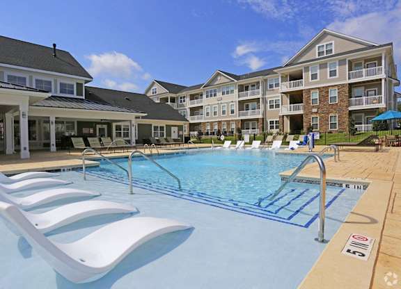 a swimming pool with white chairs in front of an apartment building
