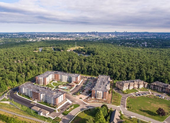 an aerial view of an apartment complex with trees and a city in the background
