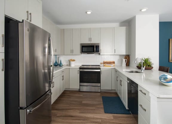 Model kitchen at Alta Clara apartments in Stoneham, MA, featuring white countertops and stainless steel appliances.