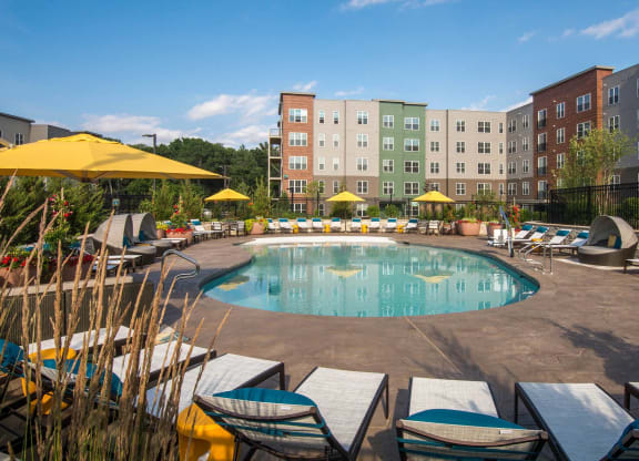 a swimming pool with chairs and umbrellas in front of an apartment building