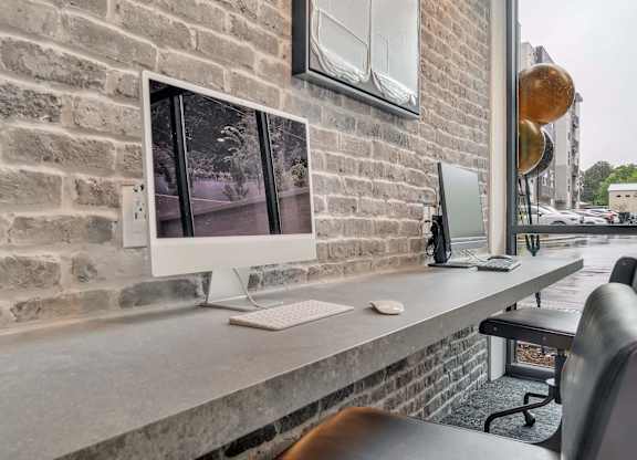 a desk with a computer on it against a brick wall