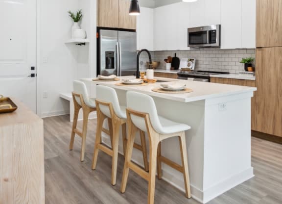 a kitchen with white cabinets and a large island with chairs at Alta City Side, Nashville, TN