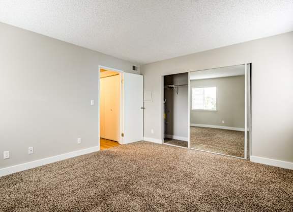 A room with a carpeted floor and a mirrored closet door.