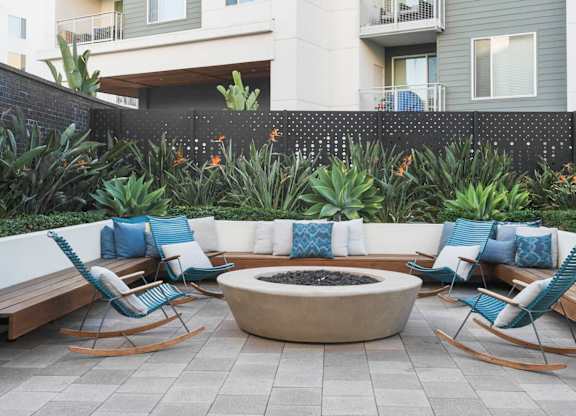 A patio with a fire pit surrounded by chairs and plants.