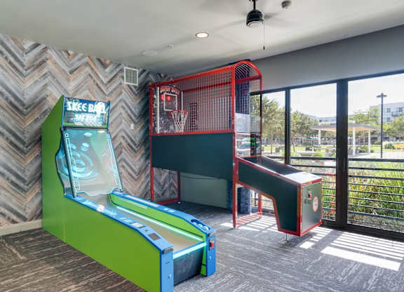 A room with a green and red arcade game and a basketball hoop.