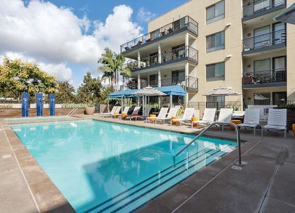 A large swimming pool in front of a building with sun loungers.