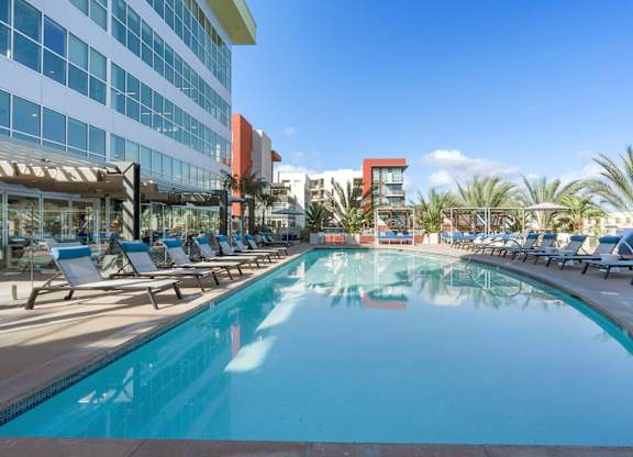 A large swimming pool with lounge chairs and a building in the background.