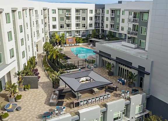 A large outdoor pool area with a table and chairs is surrounded by apartment buildings.