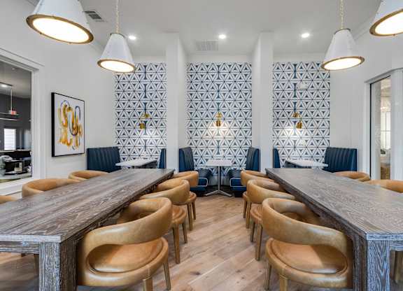A long wooden table is surrounded by chairs in a room with patterned wallpaper.