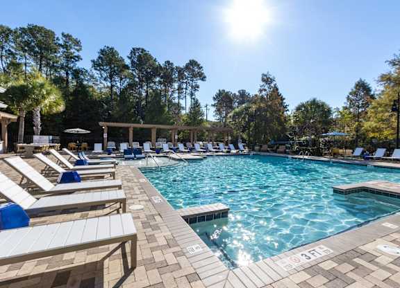 Pet-Friendly Apartments in Charleston, SC - The Avenues at Verdier Pointe - Swimming Pool Surrounded by Sun Loungers, Umbrellas, Pergolas, and Trees.