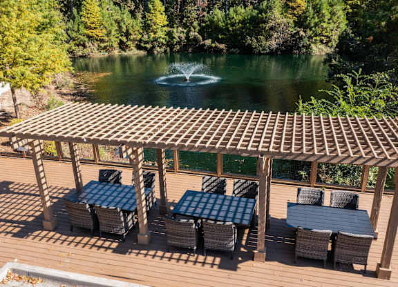 Three-Bedroom Apartments in Charleston, SC - The Avenues at Verdier Pointe - Picnic Area with Outdoor Dining Tables and Chairs, Beneath a Wooden Pergola, Overlooking a Lake and a Lush Landscaping.