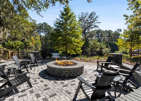 A fire pit in the middle of a brick patio surrounded by chairs.