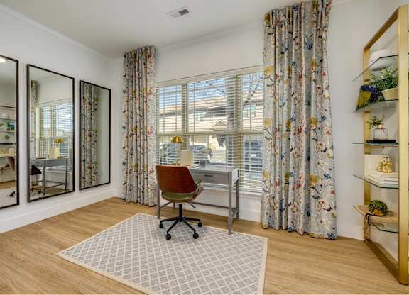 A room with a desk and a chair in front of a window with curtains.