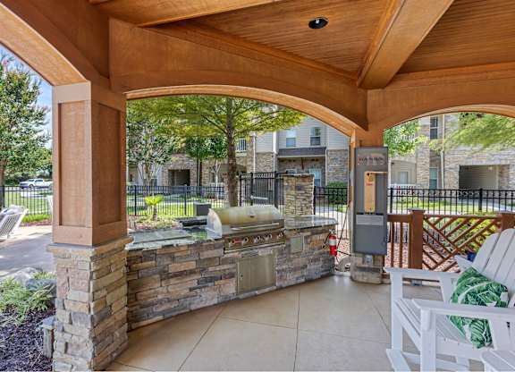 A patio with a stone wall and a grill.