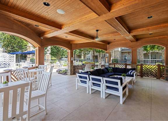 A wooden patio with white chairs and a black couch.