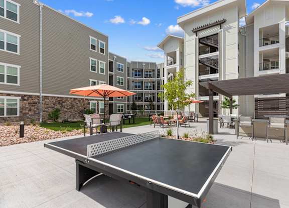 A table tennis table is in the middle of a courtyard with a building in the background.